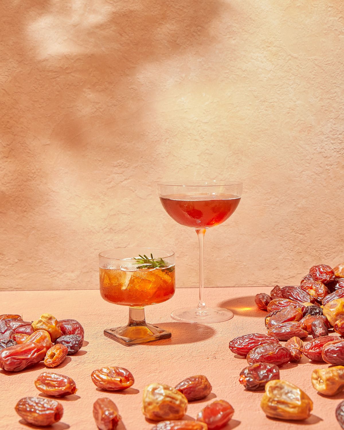A date cocktail and a spritz glowing in golden light beside a scatter of glossy dates